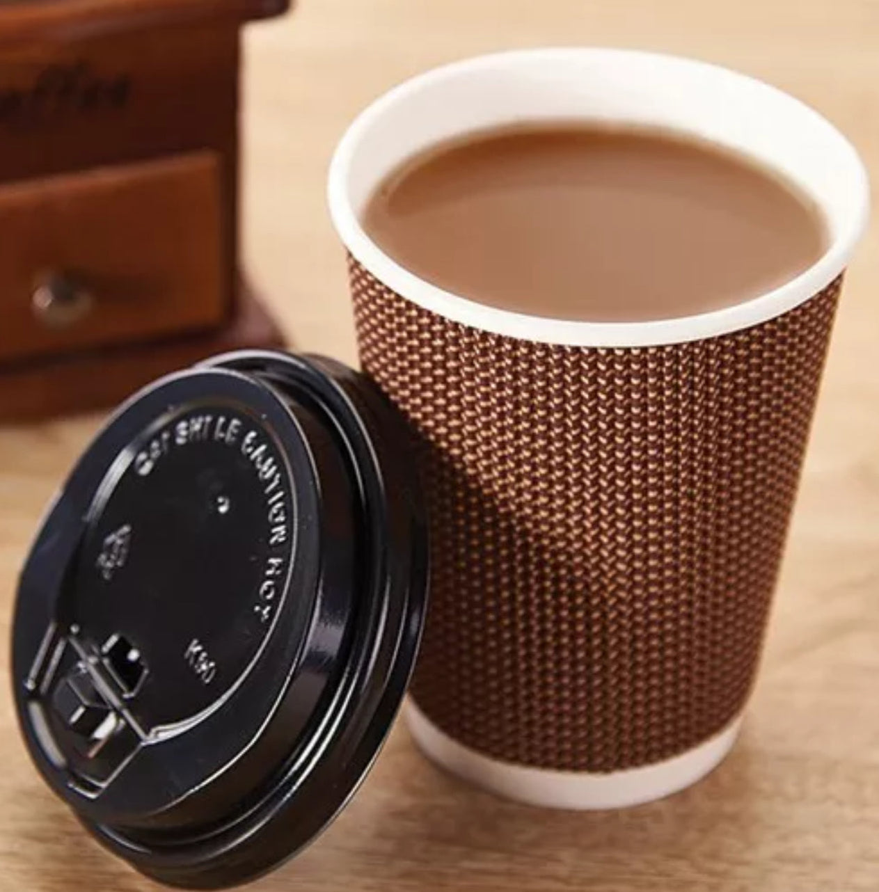 Paper cup with textured design and black lid on a wooden surface