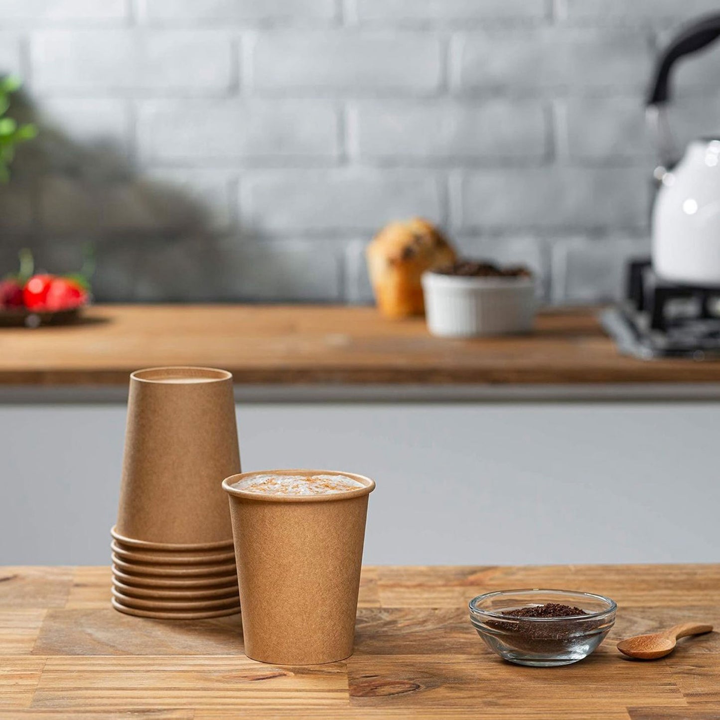 Stack of brown paper cups on a wooden table with a kitchen background.