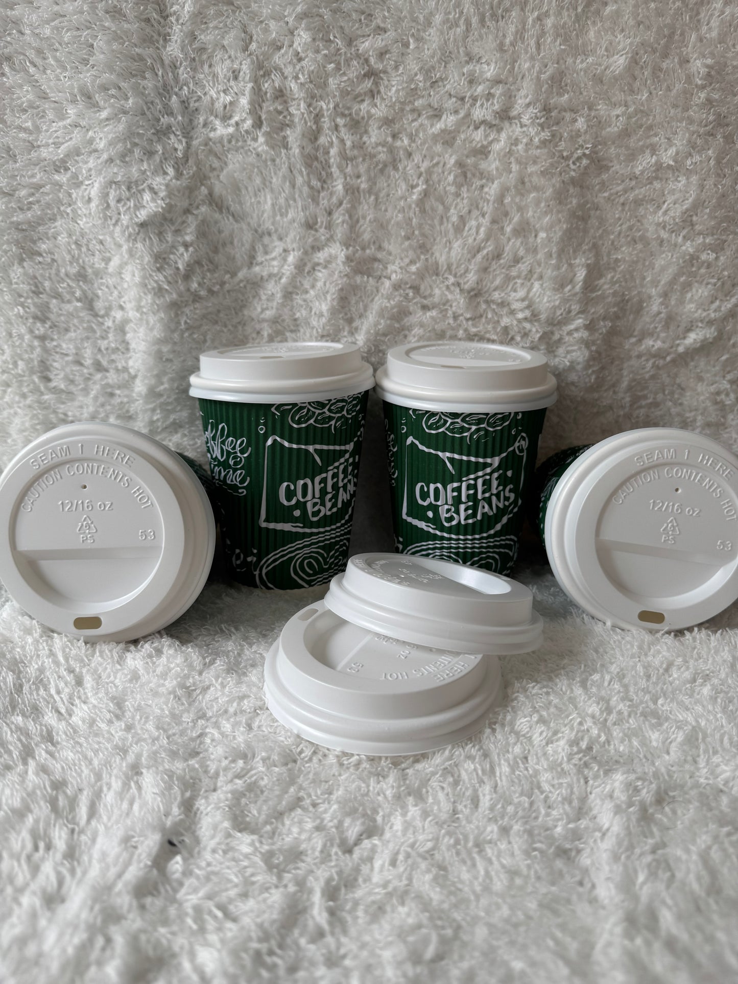 Stack of disposable coffee cups with green sleeves on a textured gray surface
