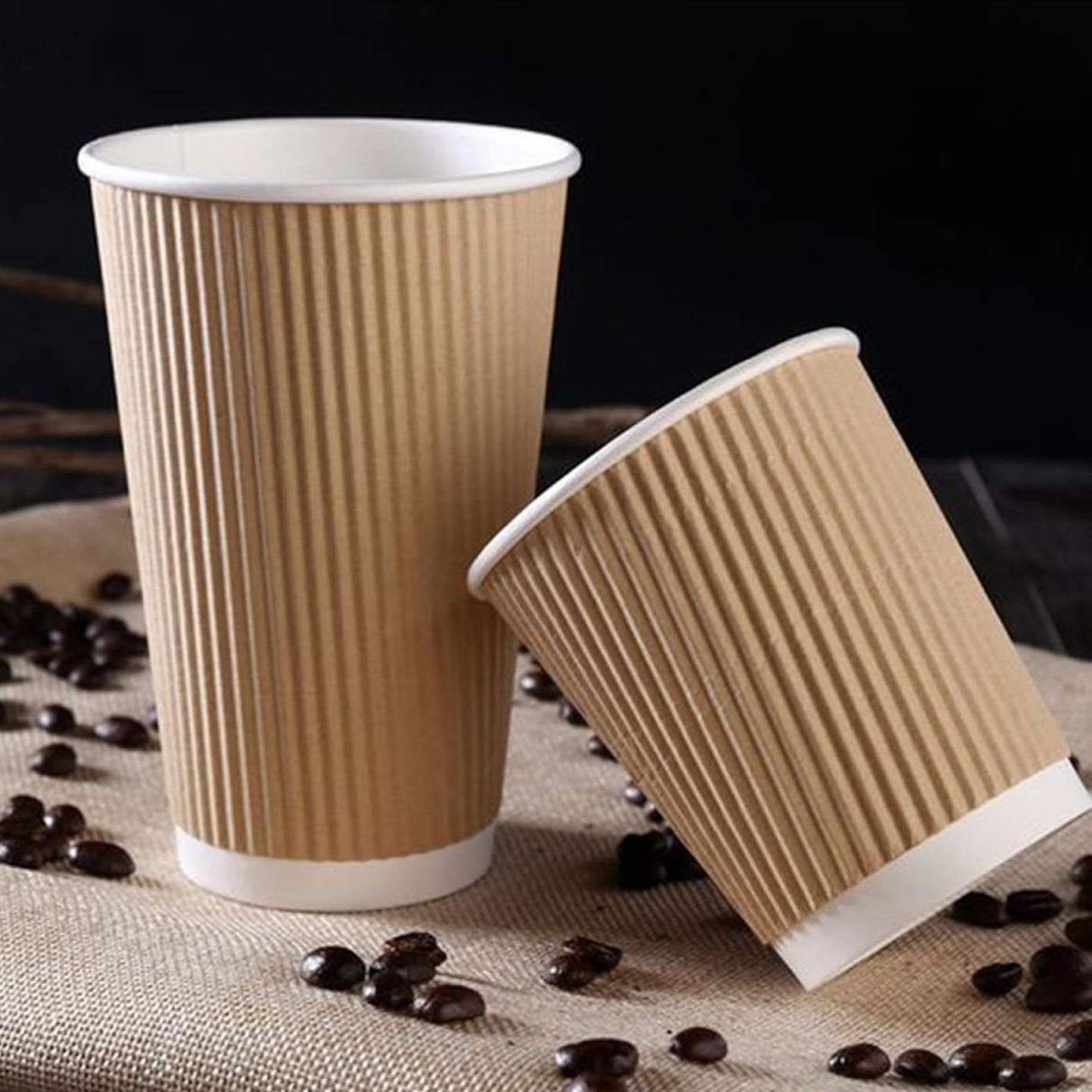 Two brown paper cups with white interiors on a surface with coffee beans.