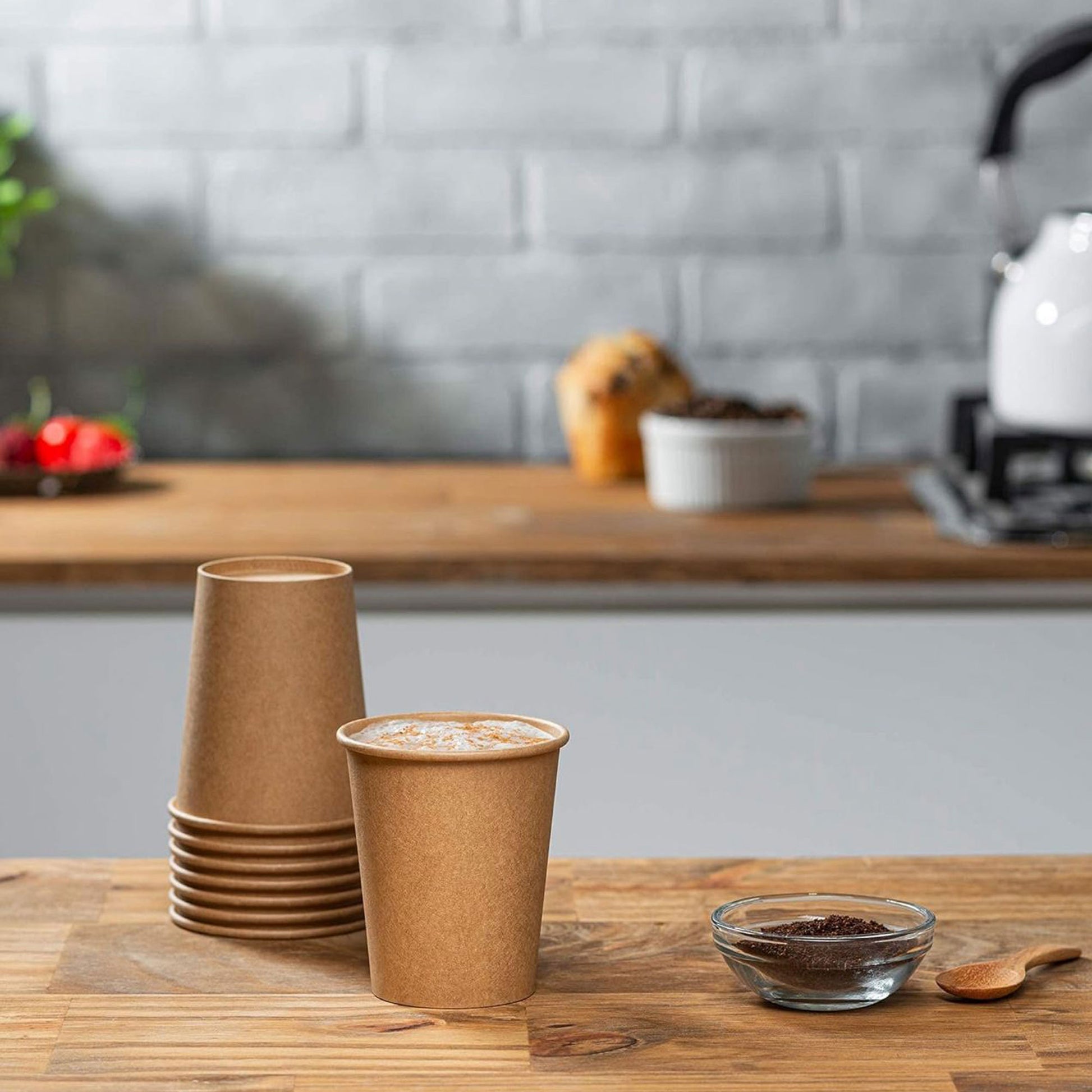 Stack of brown paper cups on a wooden table with a kitchen background.